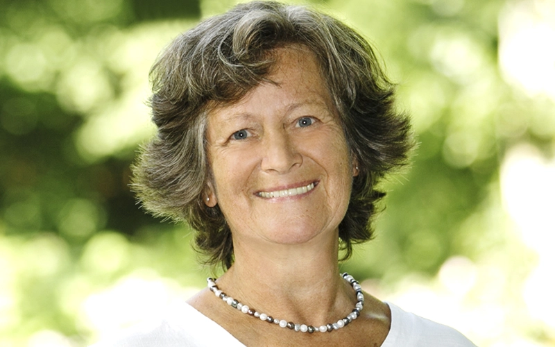 Portrait von Gabriele Donath. Einer freundlich in die Kamera lächelnden Frau mit dunklen Haaren, einer Perlenkette und weißem T-Shirt.